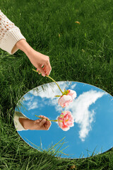 Wall Mural - nature concept - hand with peony flower and sky reflection in round mirror on summer field