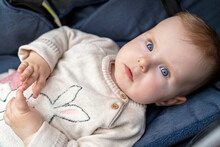 Beautiful Baby With Blue Eyes And Blonde Hair Looks At The Camera. Adorable Baby Of 10 Months In A Knitted Sweater Lies In A Stroller.