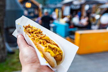 man holds fresh hot dog with sauce in hands. Street food, fast food outdoor