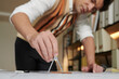 © DragonImages - Civil engineer measuring distance between two dots on building blueprint with compass