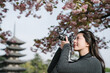 © PR Image Factory - side view taiwanese woman is taking a photo of the gorgeous scenic attraction under cherry trees. selective focus female is using camera to seize the beauty near five storied pagoda.