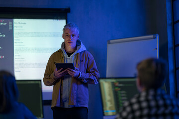 Teacher giving computer science lecture to young students in dark room. Room. Explaining Information Technology.