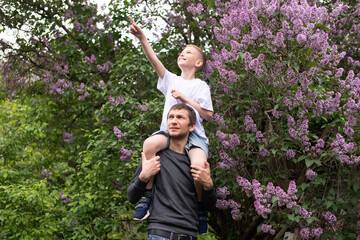 The boy is sitting on Dad's shoulders, pointing his finger to the side and laughing