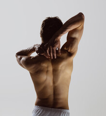 Back view of young shirtless muscled man wearing white boxer-briefs standing isolated on gray background. Natural beauty of male body