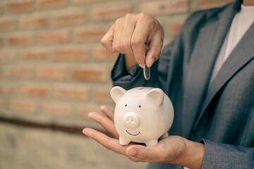 Asian businesswomen hold piggy banks and put coins in piggy banks to save money with coins to step into business, grow successful, and save money. savings concept