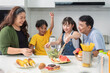 © chartphoto - A young Asian family prepares a vegetable salad for lunch on the kitchen table with excited and happy smiles. Parents teach daughter and son to cook at home.