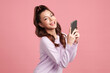 Beautiful young asian women smiling with smartphone chatting with partners online on pink background,