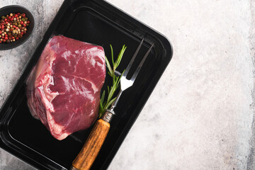 Wall Mural - Beef steak. Fresh raw beef steak with fork and rosemary in vacuum black plastic pack on grey stone background. Vacoom package. Top view. Mockup for design idea.