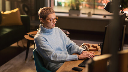 Young Beautiful Woman Working from Home on Desktop Computer in Sunny Stylish Loft Apartment. Creative Female Checking Social Media, Browsing Internet. Urban City View from Big Window.