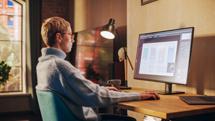 Fototapete - Young Attractive Woman Working from Home on Desktop Computer in Sunny Stylish Loft Apartment. Creative Designer Wearing Cozy Blue Sweater and Glasses. Urban City View from Big Window.