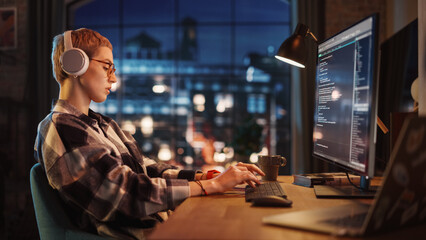Aufkleber - Young Woman Writing Code on Desktop Computer in Stylish Loft Apartment in the Evening. Creative Female Wearing Headphones, Working from Home on Software Development. Urban City View from Big Window.