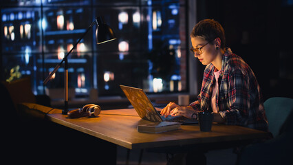 Wall Mural - Young Beuatiful Women Working from Home on Laptop Computer in Stylish Loft Apartment in the Evening. Creative Female Wearing Cozy Casual Outfit. Urban City View from Big Window.