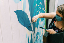 Female Artist Painting A Mural On Wall Of Local Business
