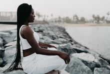 Woman With Braids Sittingon The Rocks At The Beach Meditating