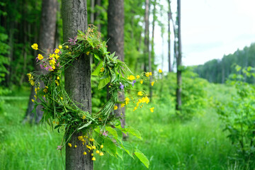 Wall Mural - wreath of wildflowers hanging on tree in forest, natural abstract green background. wreath - floral traditional decor, symbol of Summer Solstice Day, Midsummer. pagan witch traditions, wiccan ritual.