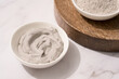 Bowl with gray cosmetic clay cream on wooden tray - mineral bentonite facial mask. Skincare beauty concept