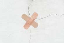 A Crosswise Of Two Bandage Is Stuck To A Crack In The Concrete Wall. The Concept Of Recovery Or Treatment