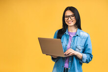 Portrait Of Happy Young Beautiful Surprised Woman With Glasses Standing With Laptop Isolated On Yellow Background. Space For Text.