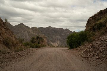 Wall Mural - Travel. View of the dirt road across the desert and mountains under a cloudy sky.