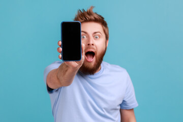 Wall Mural - portrait of bearded man holding out cellphone and looking at camera with big eyes and open mouth, sa