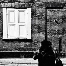 A Black And White Street Image Of A Woman Walking And Taking On Her Mobile Phone Past A Historic Old House. Hull Old Town, UK 