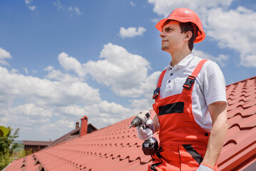 Wall Mural - Man worker master in red overall and helmet is fixing the metal tile roof.