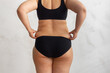 © Юля Бурмистрова - Cropped rearview of fat, adipose, overweight female body in black underwear, checking and holding excess folds, sides on back. Cellulite friable skin problem. Dieting and unhealthy eating problem