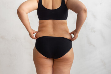 Wall Mural - Cropped rearview of fat, adipose, overweight female body in black underwear, checking and holding excess folds, sides on back. Cellulite friable skin problem. Dieting and unhealthy eating problem