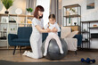 © sofiko14 - Happy fitness family training on swiss ball in living room. Portrait of sporty positive caucasian mother enjoying home fitness activity with her little cute girl sitting on rubber fitball.