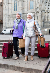 Senior woman with female friend travelling together, walking with baggage on city