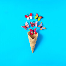 An Ice Cream Cone With Colorful Butterflies Flying Out Against Pastel Blue Background. Minimal  Concept For Summer Season Holidays And Leisure. Design For Seasonal Banner, Card Or Print. Copy Space. 