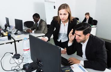 Wall Mural - Unhappy man manager working at laptop and angry woman boss pointinting to misses in work. Focus on man