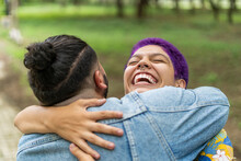 Imagen De Un Hombre Homosexual De Espaldas Abrazando A Una Mujer Con El Cabello Corto Y Pintado De Color Morado, Por Una Zona Verde.