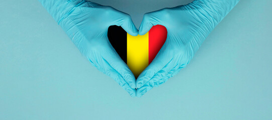 Doctors hands wearing blue surgical gloves making hear shape symbol with Belgium flag