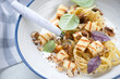 Closeup of creamy pasta with chopped halloumi cheese, walnuts and fresh basil served in a white plate