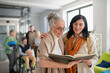 © Halfpoint - Happy mature woman student with book discussing with teacher in corridor in university.
