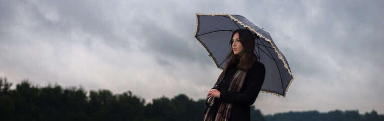 Wall Mural - Young woman walking in the rain on a cloudy autumn day