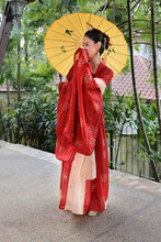 Young Attractive Asian Woman Wearing Tadeonal Chinese Red Hanfu Long Skirt Dress Costume Scarf Hairpin Earing Decorated Umbrella Outdoor Green Garden Patio