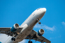 Low Angle View Of Commercial Airline Flight Taking Off Or Landing Taking Passengers On International Journeys For Vacation, Holidays And Adventure. Blue Sky And Some White Clouds Behind