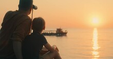 Fun Father And Son Of Traveler Sitting On Sea Beach With Binoculars Under Sunset Sky In Evening Time. Family Relaxing Enjoying Holidays, Travel Day. 4K Video