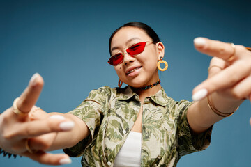 Portrait of trendy teenage girl wearing colored sunglasses and gesturing over vibrant blue background