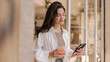 © Look! - Pretty young caucasian woman is browsing email standing in doorway with glass of juice. Brunette wears top, shirt and pants. Cell phone usage concept