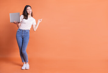 Full length image of young Asian girl using laptop on orange background