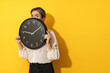 Businesswoman peeking out from behind big clock on a yellow background