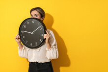 Businesswoman Peeking Out From Behind Big Clock On A Yellow Background