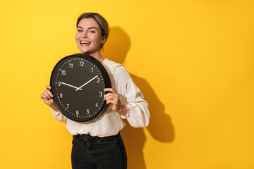 Cheerful woman holding big clock on yellow background