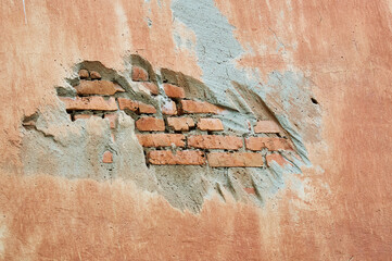 The texture of a building cladding with a piece falling out with a gap on a crumbling brick wall. Terracotta color of the outer wall. Old building with peeling plaster. Traces of power tools.