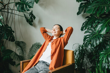 Wall Mural - A relaxed young woman is relaxing while sitting in the beautiful garden of the house. A female florist, gardener is resting after taking care of houseplants in the home garden. Work-life balance.