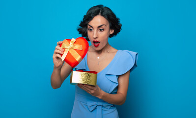 Wall Mural - Women's day. St. Valentine's day. Birthday. Holidays. Close up portrait of elegant excited happy woman in dress with gift box in hands isolated on blue background