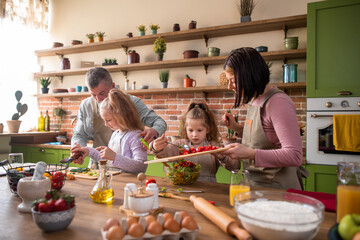 Happy family time for a young family mom dad and two cute girls preparing together healthy dinner at amazing kitchen island they smiling large and feeling excited.